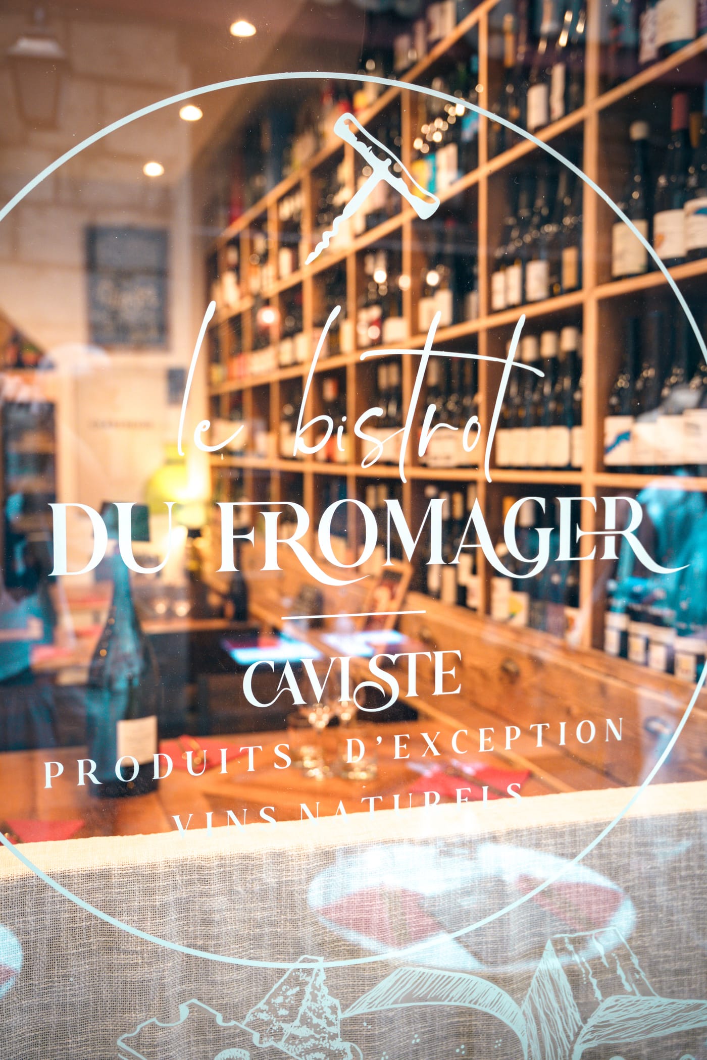 Vitrine du Bistrot du Fromager rue Droite, logo gravé sur la vitre et cave à vins en fond